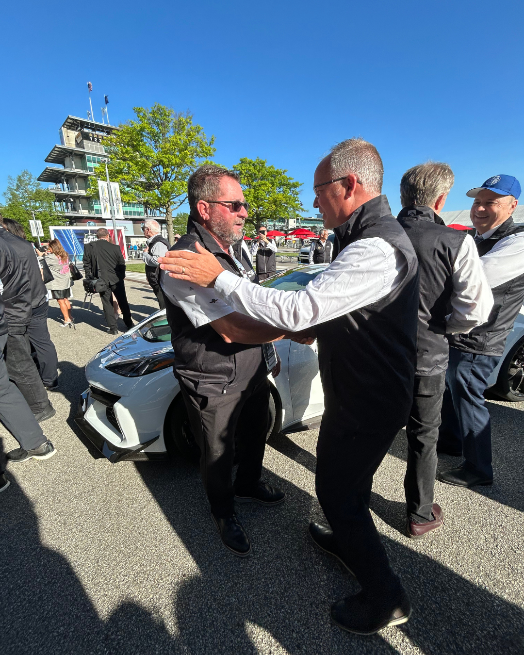 Mayor furgeson shaking hands with another mayor with indy car and pagoda in background no clouds